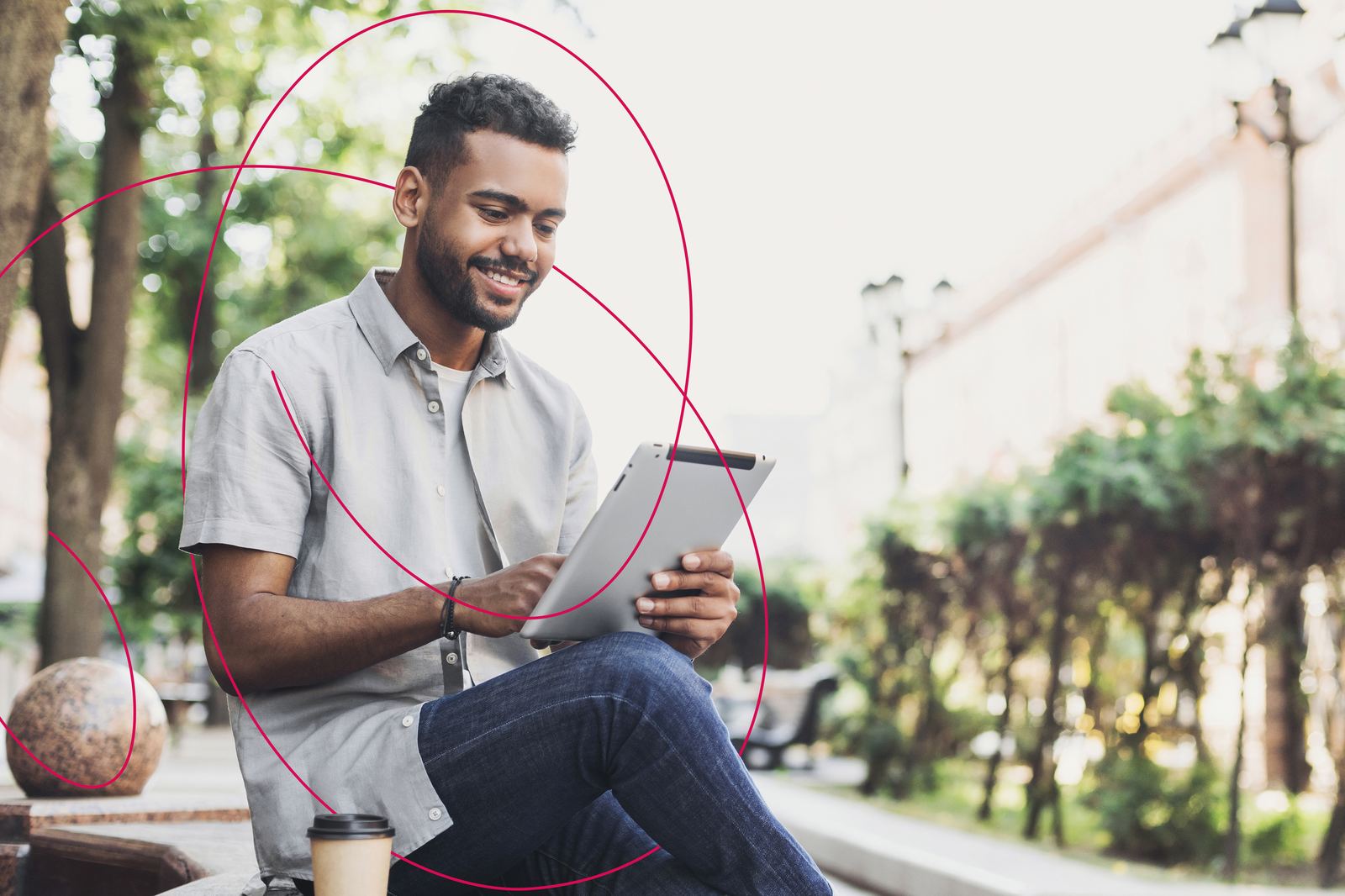 A young man sitting outdoors smiling at his tablet
